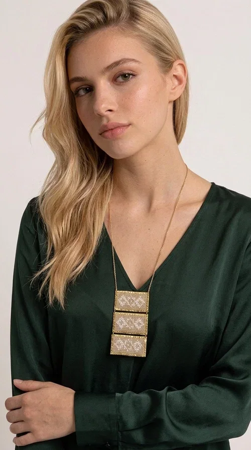 , The statement embroidered ivory necklace is a handmade creation that combines the traditional art of embroidery with a contemporary jewelry aesthetic, adding a unique, eye-catching touch to any outfit.

Designed by Greek Jewelry Designer Aikaterini Chalkiadaki, this necklace features three rectangular embroidered sections with ivory geometric motifs and gold details set in a brass frame. It hangs from a delicate gold chain that lends elegance and lightness, while the folklore-style geometric patterns give the piece a distinctive, ethnographic character. The combination of brass and fabric creates an intriguing contrast of materials that draws the eye.

Ideal for both day and evening wear, it pairs beautifully with white or monochrome outfits to highlight its geometric patterns. The ivory color makes it versatile and timeless, perfect for summer looks as well as formal or business occasions.