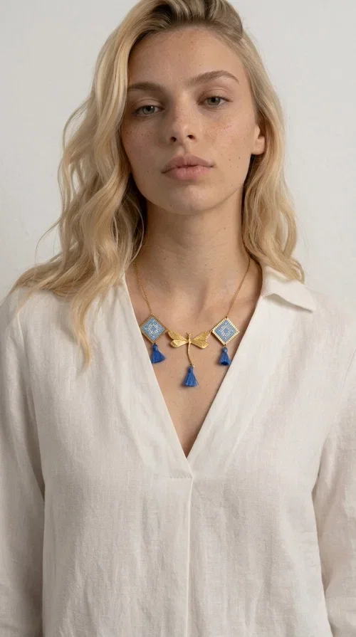, A statement necklace that combines the tradition of embroidery art with contemporary aesthetics — ideal for those who want to stand out with style and character.

Designed by Greek Jewelry Designer Aikaterini Chalkiadaki, this handmade embroidered necklace in light blue brings to the forefront the magic of geometric patterns inspired by Greek folk tradition. Fabric rhombuses with finely worked embroidery in light blue and white shades alternate with a golden dragonfly made of brass, while four hanging tassels in deep blue add movement and vibrancy to the composition. The golden brass chain completes a creation full of color, texture and atmosphere.

Wear it over a white shirt or a simple monochrome dress to highlight all its beauty. It fits perfectly with summer looks, romantic evening outings, and boho-chic day looks as well. It is also an excellent gift choice for a woman who loves striking, handmade jewelry.