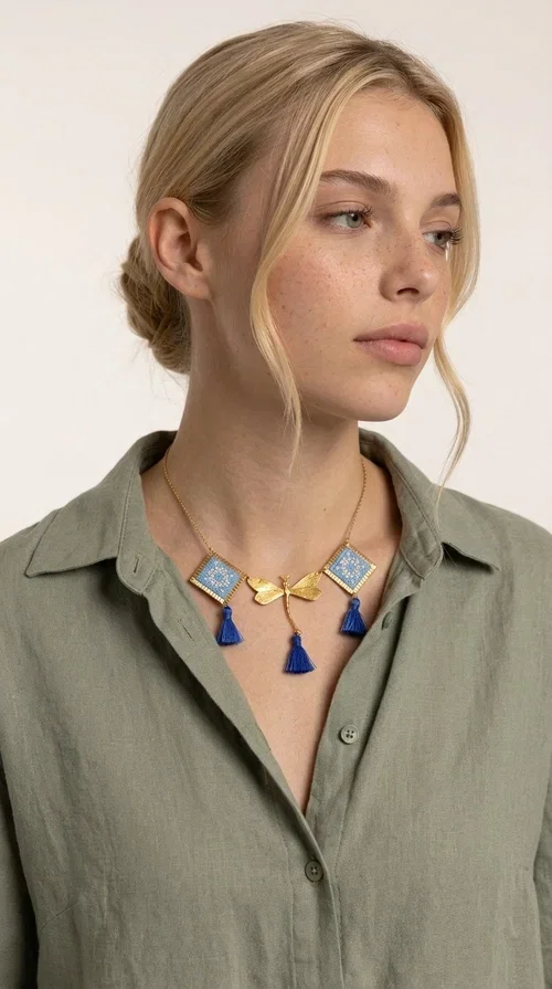, A statement necklace that combines the tradition of embroidery art with contemporary aesthetics — ideal for those who want to stand out with style and character.

Designed by Greek Jewelry Designer Aikaterini Chalkiadaki, this handmade embroidered necklace in light blue brings to the forefront the magic of geometric patterns inspired by Greek folk tradition. Fabric rhombuses with finely worked embroidery in light blue and white shades alternate with a golden dragonfly made of brass, while four hanging tassels in deep blue add movement and vibrancy to the composition. The golden brass chain completes a creation full of color, texture and atmosphere.

Wear it over a white shirt or a simple monochrome dress to highlight all its beauty. It fits perfectly with summer looks, romantic evening outings, and boho-chic day looks as well. It is also an excellent gift choice for a woman who loves striking, handmade jewelry.
