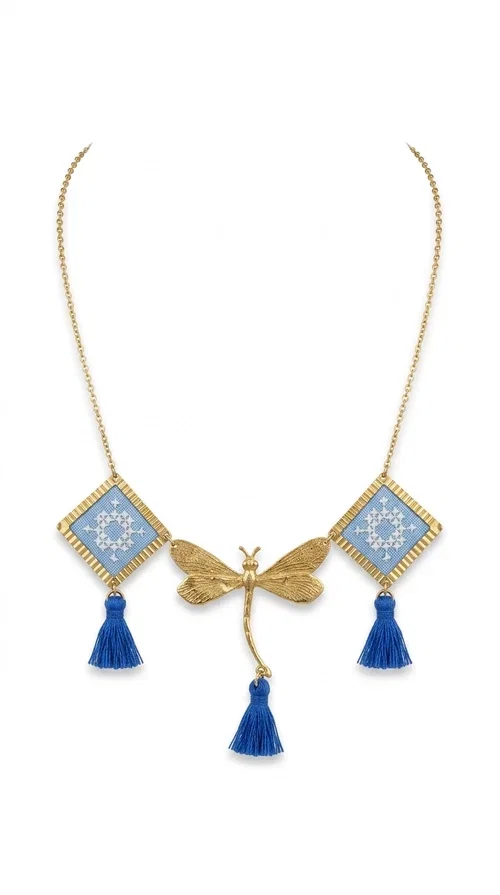 , A statement necklace that combines the tradition of embroidery art with contemporary aesthetics — ideal for those who want to stand out with style and character.

Designed by Greek Jewelry Designer Aikaterini Chalkiadaki, this handmade embroidered necklace in light blue brings to the forefront the magic of geometric patterns inspired by Greek folk tradition. Fabric rhombuses with finely worked embroidery in light blue and white shades alternate with a golden dragonfly made of brass, while four hanging tassels in deep blue add movement and vibrancy to the composition. The golden brass chain completes a creation full of color, texture and atmosphere.

Wear it over a white shirt or a simple monochrome dress to highlight all its beauty. It fits perfectly with summer looks, romantic evening outings, and boho-chic day looks as well. It is also an excellent gift choice for a woman who loves striking, handmade jewelry.