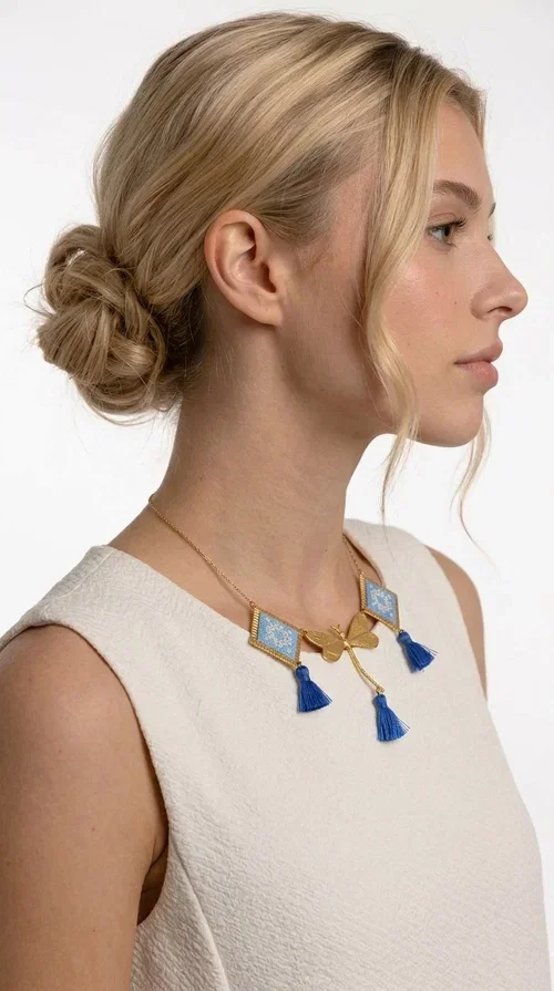 , A statement necklace that combines the tradition of embroidery art with contemporary aesthetics — ideal for those who want to stand out with style and character.

Designed by Greek Jewelry Designer Aikaterini Chalkiadaki, this handmade embroidered necklace in light blue brings to the forefront the magic of geometric patterns inspired by Greek folk tradition. Fabric rhombuses with finely worked embroidery in light blue and white shades alternate with a golden dragonfly made of brass, while four hanging tassels in deep blue add movement and vibrancy to the composition. The golden brass chain completes a creation full of color, texture and atmosphere.

Wear it over a white shirt or a simple monochrome dress to highlight all its beauty. It fits perfectly with summer looks, romantic evening outings, and boho-chic day looks as well. It is also an excellent gift choice for a woman who loves striking, handmade jewelry.