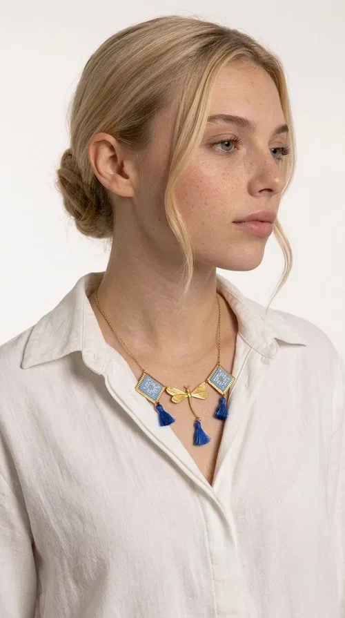 , A statement necklace that combines the tradition of embroidery art with contemporary aesthetics — ideal for those who want to stand out with style and character.

Designed by Greek Jewelry Designer Aikaterini Chalkiadaki, this handmade embroidered necklace in light blue brings to the forefront the magic of geometric patterns inspired by Greek folk tradition. Fabric rhombuses with finely worked embroidery in light blue and white shades alternate with a golden dragonfly made of brass, while four hanging tassels in deep blue add movement and vibrancy to the composition. The golden brass chain completes a creation full of color, texture and atmosphere.

Wear it over a white shirt or a simple monochrome dress to highlight all its beauty. It fits perfectly with summer looks, romantic evening outings, and boho-chic day looks as well. It is also an excellent gift choice for a woman who loves striking, handmade jewelry.