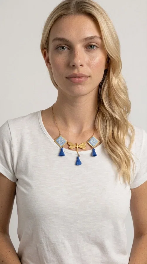 , A statement necklace that combines the tradition of embroidery art with contemporary aesthetics — ideal for those who want to stand out with style and character.

Designed by Greek Jewelry Designer Aikaterini Chalkiadaki, this handmade embroidered necklace in light blue brings to the forefront the magic of geometric patterns inspired by Greek folk tradition. Fabric rhombuses with finely worked embroidery in light blue and white shades alternate with a golden dragonfly made of brass, while four hanging tassels in deep blue add movement and vibrancy to the composition. The golden brass chain completes a creation full of color, texture and atmosphere.

Wear it over a white shirt or a simple monochrome dress to highlight all its beauty. It fits perfectly with summer looks, romantic evening outings, and boho-chic day looks as well. It is also an excellent gift choice for a woman who loves striking, handmade jewelry.