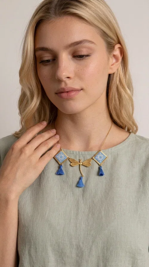 , A statement necklace that combines the tradition of embroidery art with contemporary aesthetics — ideal for those who want to stand out with style and character.

Designed by Greek Jewelry Designer Aikaterini Chalkiadaki, this handmade embroidered necklace in light blue brings to the forefront the magic of geometric patterns inspired by Greek folk tradition. Fabric rhombuses with finely worked embroidery in light blue and white shades alternate with a golden dragonfly made of brass, while four hanging tassels in deep blue add movement and vibrancy to the composition. The golden brass chain completes a creation full of color, texture and atmosphere.

Wear it over a white shirt or a simple monochrome dress to highlight all its beauty. It fits perfectly with summer looks, romantic evening outings, and boho-chic day looks as well. It is also an excellent gift choice for a woman who loves striking, handmade jewelry.