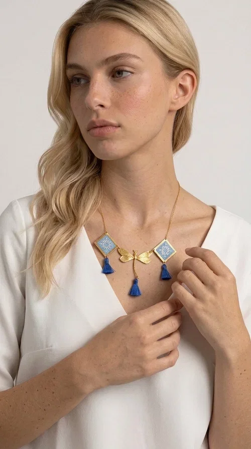 , A statement necklace that combines the tradition of embroidery art with contemporary aesthetics — ideal for those who want to stand out with style and character.

Designed by Greek Jewelry Designer Aikaterini Chalkiadaki, this handmade embroidered necklace in light blue brings to the forefront the magic of geometric patterns inspired by Greek folk tradition. Fabric rhombuses with finely worked embroidery in light blue and white shades alternate with a golden dragonfly made of brass, while four hanging tassels in deep blue add movement and vibrancy to the composition. The golden brass chain completes a creation full of color, texture and atmosphere.

Wear it over a white shirt or a simple monochrome dress to highlight all its beauty. It fits perfectly with summer looks, romantic evening outings, and boho-chic day looks as well. It is also an excellent gift choice for a woman who loves striking, handmade jewelry.