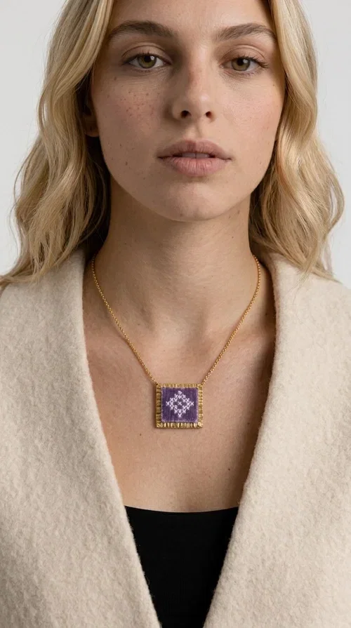 , The embroidered lilac necklace with geometric patterns is a statement piece that combines the traditional art of embroidery with a modern aesthetic, creating a result that instantly stands out. Designed by Greek Jewelry Designer Aikaterini Chalkiadaki, this handmade necklace is the perfect blend of folklore inspiration and contemporary style.

The rectangular pendant in lilac shades features detailed geometric motifs embroidered on fabric, framed by gold-tone brass that adds elegance and structure. The gold box chain harmoniously completes the look, while the larger size of the pendant makes it ideal for those who want to make a statement with their style.

Wear it with casual or formal outfits — it pairs equally well with a linen dress for a summer stroll and a blazer for a professional look. An ideal gift for every woman who loves unique, handmade jewelry with a Greek soul.