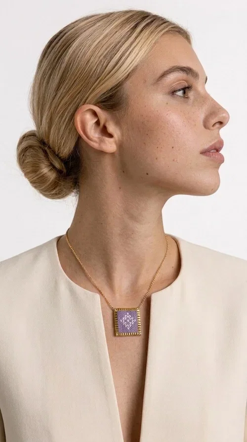 , The embroidered lilac necklace with geometric patterns is a statement piece that combines the traditional art of embroidery with a modern aesthetic, creating a result that instantly stands out. Designed by Greek Jewelry Designer Aikaterini Chalkiadaki, this handmade necklace is the perfect blend of folklore inspiration and contemporary style.

The rectangular pendant in lilac shades features detailed geometric motifs embroidered on fabric, framed by gold-tone brass that adds elegance and structure. The gold box chain harmoniously completes the look, while the larger size of the pendant makes it ideal for those who want to make a statement with their style.

Wear it with casual or formal outfits — it pairs equally well with a linen dress for a summer stroll and a blazer for a professional look. An ideal gift for every woman who loves unique, handmade jewelry with a Greek soul.