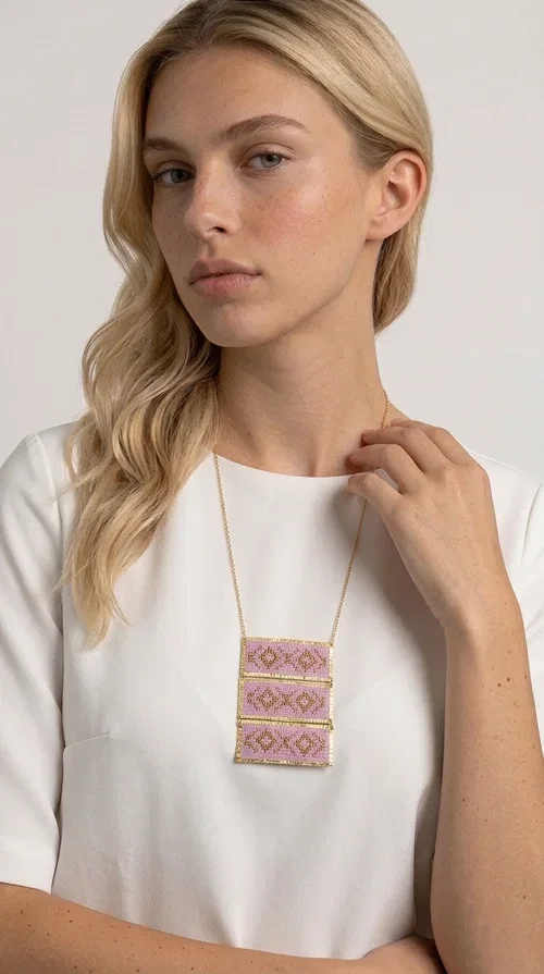 , An embroidered necklace that combines tradition with contemporary aesthetics — the Statement Embroidered Necklace in Lilac with Geometric Patterns is the jewel that turns any look into a style statement. Designed by Greek Jewelry Designer Aikaterini Chalkiadaki, this long necklace carries the distinctive energy of folklore aesthetics in a bold, striking version.

Three rectangular brass plates in a gold hue are covered with handmade embroidery in lilac and gold tones, featuring repeating geometric motifs inspired by Greek tradition. They hang from a delicate gold chain, creating a long necklace with a statement presence that suits both casual and elegant looks.

Ideal to pair with linen, cotton or evening wear, this necklace adds character to any outfit — from summer outings to formal occasions. The lilac hue is romantic and versatile, while the geometric patterns bring a strong personality.