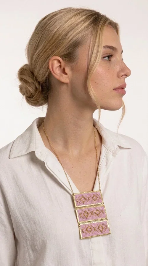 , An embroidered necklace that combines tradition with contemporary aesthetics — the Statement Embroidered Necklace in Lilac with Geometric Patterns is the jewel that turns any look into a style statement. Designed by Greek Jewelry Designer Aikaterini Chalkiadaki, this long necklace carries the distinctive energy of folklore aesthetics in a bold, striking version.

Three rectangular brass plates in a gold hue are covered with handmade embroidery in lilac and gold tones, featuring repeating geometric motifs inspired by Greek tradition. They hang from a delicate gold chain, creating a long necklace with a statement presence that suits both casual and elegant looks.

Ideal to pair with linen, cotton or evening wear, this necklace adds character to any outfit — from summer outings to formal occasions. The lilac hue is romantic and versatile, while the geometric patterns bring a strong personality.