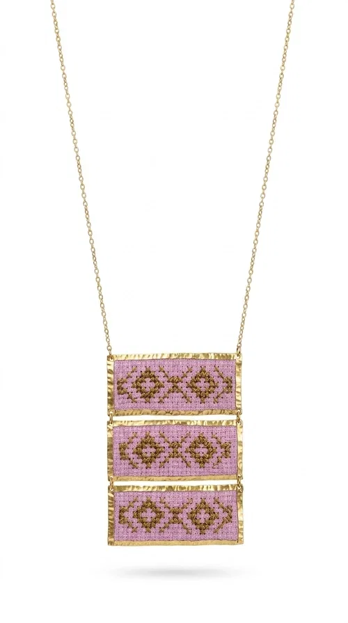 , An embroidered necklace that combines tradition with contemporary aesthetics — the Statement Embroidered Necklace in Lilac with Geometric Patterns is the jewel that turns any look into a style statement. Designed by Greek Jewelry Designer Aikaterini Chalkiadaki, this long necklace carries the distinctive energy of folklore aesthetics in a bold, striking version.

Three rectangular brass plates in a gold hue are covered with handmade embroidery in lilac and gold tones, featuring repeating geometric motifs inspired by Greek tradition. They hang from a delicate gold chain, creating a long necklace with a statement presence that suits both casual and elegant looks.

Ideal to pair with linen, cotton or evening wear, this necklace adds character to any outfit — from summer outings to formal occasions. The lilac hue is romantic and versatile, while the geometric patterns bring a strong personality.