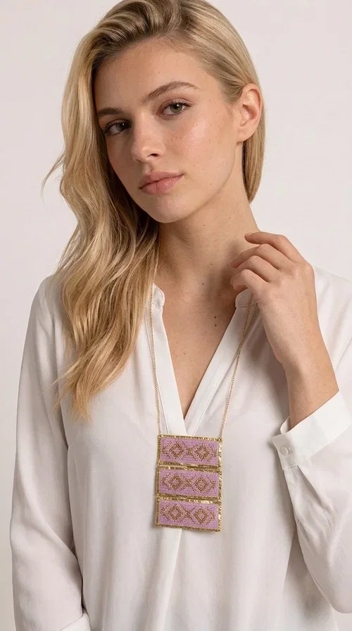 , An embroidered necklace that combines tradition with contemporary aesthetics — the Statement Embroidered Necklace in Lilac with Geometric Patterns is the jewel that turns any look into a style statement. Designed by Greek Jewelry Designer Aikaterini Chalkiadaki, this long necklace carries the distinctive energy of folklore aesthetics in a bold, striking version.

Three rectangular brass plates in a gold hue are covered with handmade embroidery in lilac and gold tones, featuring repeating geometric motifs inspired by Greek tradition. They hang from a delicate gold chain, creating a long necklace with a statement presence that suits both casual and elegant looks.

Ideal to pair with linen, cotton or evening wear, this necklace adds character to any outfit — from summer outings to formal occasions. The lilac hue is romantic and versatile, while the geometric patterns bring a strong personality.
