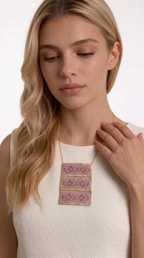 , An embroidered necklace that combines tradition with contemporary aesthetics — the Statement Embroidered Necklace in Lilac with Geometric Patterns is the jewel that turns any look into a style statement. Designed by Greek Jewelry Designer Aikaterini Chalkiadaki, this long necklace carries the distinctive energy of folklore aesthetics in a bold, striking version.

Three rectangular brass plates in a gold hue are covered with handmade embroidery in lilac and gold tones, featuring repeating geometric motifs inspired by Greek tradition. They hang from a delicate gold chain, creating a long necklace with a statement presence that suits both casual and elegant looks.

Ideal to pair with linen, cotton or evening wear, this necklace adds character to any outfit — from summer outings to formal occasions. The lilac hue is romantic and versatile, while the geometric patterns bring a strong personality.