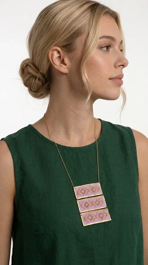 , An embroidered necklace that combines tradition with contemporary aesthetics — the Statement Embroidered Necklace in Lilac with Geometric Patterns is the jewel that turns any look into a style statement. Designed by Greek Jewelry Designer Aikaterini Chalkiadaki, this long necklace carries the distinctive energy of folklore aesthetics in a bold, striking version.

Three rectangular brass plates in a gold hue are covered with handmade embroidery in lilac and gold tones, featuring repeating geometric motifs inspired by Greek tradition. They hang from a delicate gold chain, creating a long necklace with a statement presence that suits both casual and elegant looks.

Ideal to pair with linen, cotton or evening wear, this necklace adds character to any outfit — from summer outings to formal occasions. The lilac hue is romantic and versatile, while the geometric patterns bring a strong personality.