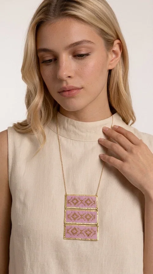 , An embroidered necklace that combines tradition with contemporary aesthetics — the Statement Embroidered Necklace in Lilac with Geometric Patterns is the jewel that turns any look into a style statement. Designed by Greek Jewelry Designer Aikaterini Chalkiadaki, this long necklace carries the distinctive energy of folklore aesthetics in a bold, striking version.

Three rectangular brass plates in a gold hue are covered with handmade embroidery in lilac and gold tones, featuring repeating geometric motifs inspired by Greek tradition. They hang from a delicate gold chain, creating a long necklace with a statement presence that suits both casual and elegant looks.

Ideal to pair with linen, cotton or evening wear, this necklace adds character to any outfit — from summer outings to formal occasions. The lilac hue is romantic and versatile, while the geometric patterns bring a strong personality.