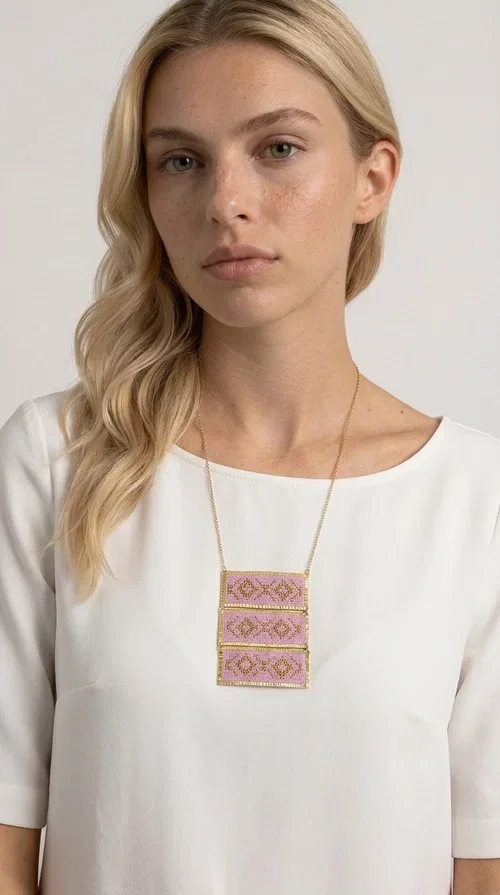 , An embroidered necklace that combines tradition with contemporary aesthetics — the Statement Embroidered Necklace in Lilac with Geometric Patterns is the jewel that turns any look into a style statement. Designed by Greek Jewelry Designer Aikaterini Chalkiadaki, this long necklace carries the distinctive energy of folklore aesthetics in a bold, striking version.

Three rectangular brass plates in a gold hue are covered with handmade embroidery in lilac and gold tones, featuring repeating geometric motifs inspired by Greek tradition. They hang from a delicate gold chain, creating a long necklace with a statement presence that suits both casual and elegant looks.

Ideal to pair with linen, cotton or evening wear, this necklace adds character to any outfit — from summer outings to formal occasions. The lilac hue is romantic and versatile, while the geometric patterns bring a strong personality.