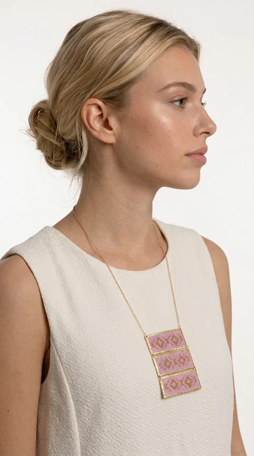 , An embroidered necklace that combines tradition with contemporary aesthetics — the Statement Embroidered Necklace in Lilac with Geometric Patterns is the jewel that turns any look into a style statement. Designed by Greek Jewelry Designer Aikaterini Chalkiadaki, this long necklace carries the distinctive energy of folklore aesthetics in a bold, striking version.

Three rectangular brass plates in a gold hue are covered with handmade embroidery in lilac and gold tones, featuring repeating geometric motifs inspired by Greek tradition. They hang from a delicate gold chain, creating a long necklace with a statement presence that suits both casual and elegant looks.

Ideal to pair with linen, cotton or evening wear, this necklace adds character to any outfit — from summer outings to formal occasions. The lilac hue is romantic and versatile, while the geometric patterns bring a strong personality.