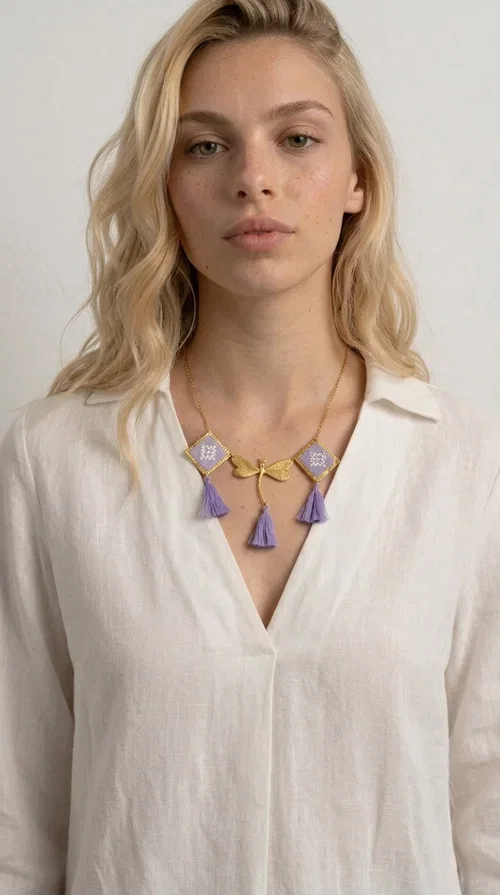 , A statement embroidered necklace that blends the traditional art of embroidery with a contemporary aesthetic — ideal for every woman who wants to express her uniqueness with style.

Designed by Greek Jewelry Designer Aikaterini Chalkiadaki, this striking necklace features two diamond-shaped pendants with handmade embroidery in shades of lilac, a gold brass facing deer (libelle) charm at the center, and four fabric tassels in lilac tones that move gracefully with every step. The gold brass chain that fastens at the back of the neck gives the piece a delicate, elegant silhouette. The geometric embroidery patterns are reminiscent of authentic Greek folk motifs, evoking the rich tradition of Greek handicraft.

Perfect for summer looks, celebrations, or everyday moments that call for something special, this handmade necklace pairs beautifully with a white shirt, a dress, or a boho outfit. Pair it with simple earrings to let it stand out to the fullest.