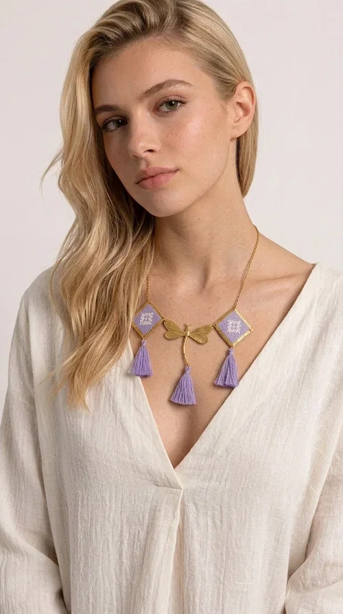 , A statement embroidered necklace that blends the traditional art of embroidery with a contemporary aesthetic — ideal for every woman who wants to express her uniqueness with style.

Designed by Greek Jewelry Designer Aikaterini Chalkiadaki, this striking necklace features two diamond-shaped pendants with handmade embroidery in shades of lilac, a gold brass facing deer (libelle) charm at the center, and four fabric tassels in lilac tones that move gracefully with every step. The gold brass chain that fastens at the back of the neck gives the piece a delicate, elegant silhouette. The geometric embroidery patterns are reminiscent of authentic Greek folk motifs, evoking the rich tradition of Greek handicraft.

Perfect for summer looks, celebrations, or everyday moments that call for something special, this handmade necklace pairs beautifully with a white shirt, a dress, or a boho outfit. Pair it with simple earrings to let it stand out to the fullest.
