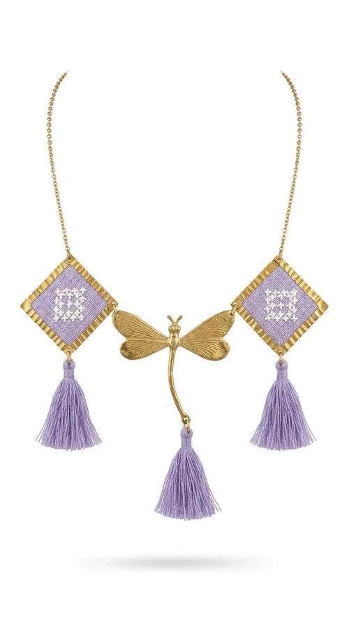 , A statement embroidered necklace that blends the traditional art of embroidery with a contemporary aesthetic — ideal for every woman who wants to express her uniqueness with style.

Designed by Greek Jewelry Designer Aikaterini Chalkiadaki, this striking necklace features two diamond-shaped pendants with handmade embroidery in shades of lilac, a gold brass facing deer (libelle) charm at the center, and four fabric tassels in lilac tones that move gracefully with every step. The gold brass chain that fastens at the back of the neck gives the piece a delicate, elegant silhouette. The geometric embroidery patterns are reminiscent of authentic Greek folk motifs, evoking the rich tradition of Greek handicraft.

Perfect for summer looks, celebrations, or everyday moments that call for something special, this handmade necklace pairs beautifully with a white shirt, a dress, or a boho outfit. Pair it with simple earrings to let it stand out to the fullest.
