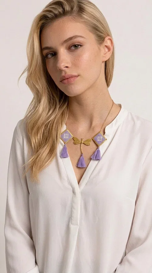 , A statement embroidered necklace that blends the traditional art of embroidery with a contemporary aesthetic — ideal for every woman who wants to express her uniqueness with style.

Designed by Greek Jewelry Designer Aikaterini Chalkiadaki, this striking necklace features two diamond-shaped pendants with handmade embroidery in shades of lilac, a gold brass facing deer (libelle) charm at the center, and four fabric tassels in lilac tones that move gracefully with every step. The gold brass chain that fastens at the back of the neck gives the piece a delicate, elegant silhouette. The geometric embroidery patterns are reminiscent of authentic Greek folk motifs, evoking the rich tradition of Greek handicraft.

Perfect for summer looks, celebrations, or everyday moments that call for something special, this handmade necklace pairs beautifully with a white shirt, a dress, or a boho outfit. Pair it with simple earrings to let it stand out to the fullest.