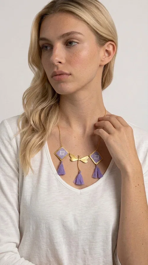 , A statement embroidered necklace that blends the traditional art of embroidery with a contemporary aesthetic — ideal for every woman who wants to express her uniqueness with style.

Designed by Greek Jewelry Designer Aikaterini Chalkiadaki, this striking necklace features two diamond-shaped pendants with handmade embroidery in shades of lilac, a gold brass facing deer (libelle) charm at the center, and four fabric tassels in lilac tones that move gracefully with every step. The gold brass chain that fastens at the back of the neck gives the piece a delicate, elegant silhouette. The geometric embroidery patterns are reminiscent of authentic Greek folk motifs, evoking the rich tradition of Greek handicraft.

Perfect for summer looks, celebrations, or everyday moments that call for something special, this handmade necklace pairs beautifully with a white shirt, a dress, or a boho outfit. Pair it with simple earrings to let it stand out to the fullest.