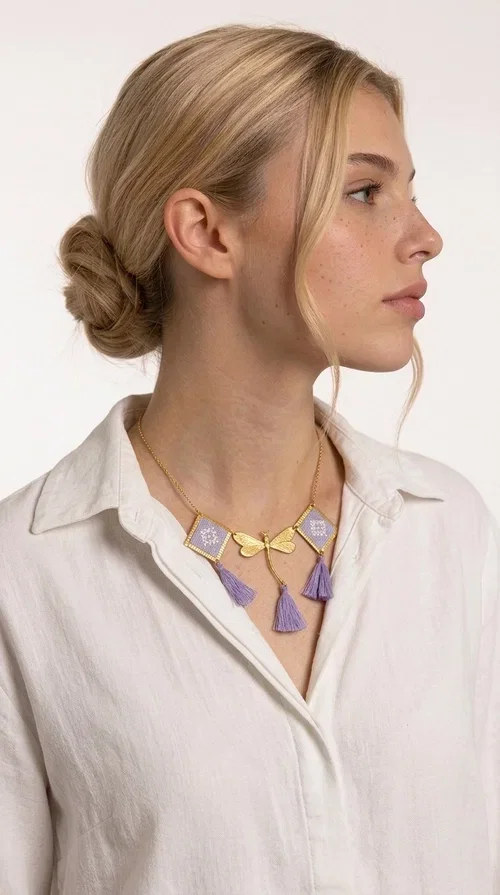 , A statement embroidered necklace that blends the traditional art of embroidery with a contemporary aesthetic — ideal for every woman who wants to express her uniqueness with style.

Designed by Greek Jewelry Designer Aikaterini Chalkiadaki, this striking necklace features two diamond-shaped pendants with handmade embroidery in shades of lilac, a gold brass facing deer (libelle) charm at the center, and four fabric tassels in lilac tones that move gracefully with every step. The gold brass chain that fastens at the back of the neck gives the piece a delicate, elegant silhouette. The geometric embroidery patterns are reminiscent of authentic Greek folk motifs, evoking the rich tradition of Greek handicraft.

Perfect for summer looks, celebrations, or everyday moments that call for something special, this handmade necklace pairs beautifully with a white shirt, a dress, or a boho outfit. Pair it with simple earrings to let it stand out to the fullest.
