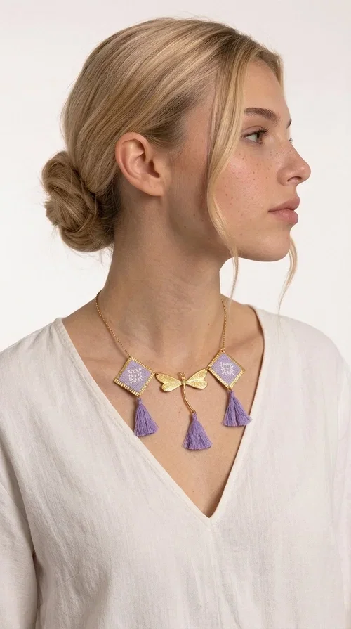 , A statement embroidered necklace that blends the traditional art of embroidery with a contemporary aesthetic — ideal for every woman who wants to express her uniqueness with style.

Designed by Greek Jewelry Designer Aikaterini Chalkiadaki, this striking necklace features two diamond-shaped pendants with handmade embroidery in shades of lilac, a gold brass facing deer (libelle) charm at the center, and four fabric tassels in lilac tones that move gracefully with every step. The gold brass chain that fastens at the back of the neck gives the piece a delicate, elegant silhouette. The geometric embroidery patterns are reminiscent of authentic Greek folk motifs, evoking the rich tradition of Greek handicraft.

Perfect for summer looks, celebrations, or everyday moments that call for something special, this handmade necklace pairs beautifully with a white shirt, a dress, or a boho outfit. Pair it with simple earrings to let it stand out to the fullest.