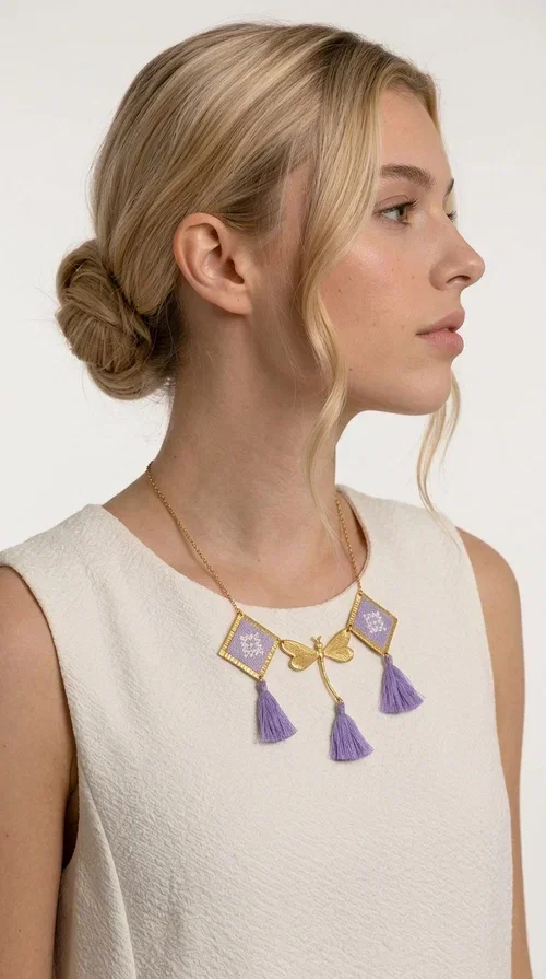 , A statement embroidered necklace that blends the traditional art of embroidery with a contemporary aesthetic — ideal for every woman who wants to express her uniqueness with style.

Designed by Greek Jewelry Designer Aikaterini Chalkiadaki, this striking necklace features two diamond-shaped pendants with handmade embroidery in shades of lilac, a gold brass facing deer (libelle) charm at the center, and four fabric tassels in lilac tones that move gracefully with every step. The gold brass chain that fastens at the back of the neck gives the piece a delicate, elegant silhouette. The geometric embroidery patterns are reminiscent of authentic Greek folk motifs, evoking the rich tradition of Greek handicraft.

Perfect for summer looks, celebrations, or everyday moments that call for something special, this handmade necklace pairs beautifully with a white shirt, a dress, or a boho outfit. Pair it with simple earrings to let it stand out to the fullest.