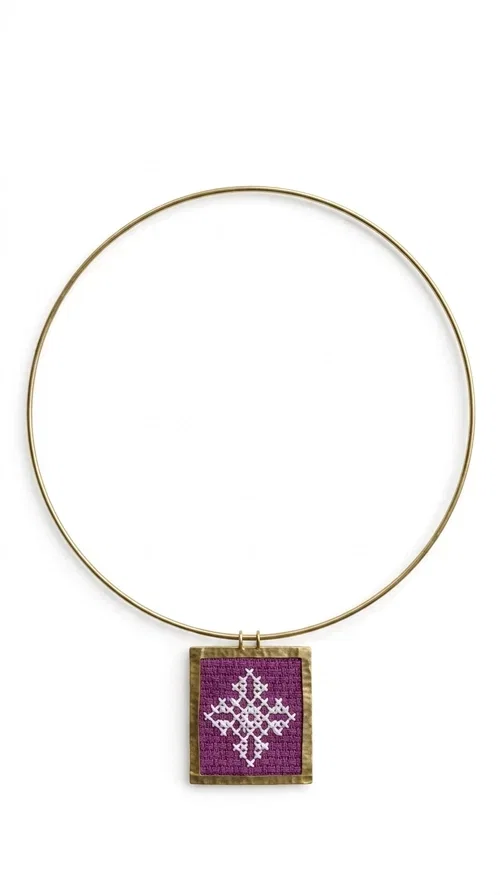 , The embroidered magenta necklace with geometric patterns is a statement piece that combines the traditional art of embroidery with a modern aesthetic — ideal for every woman who wants to express herself boldly and stylishly.

Designed by Greek Jewelry Designer Aikaterini Chalkiadaki, this handmade necklace features a square pendant in deep purple-magenta fabric, adorned with a white embroidered geometric design inspired by folk art tradition. The golden brass metal frame elegantly encases the pendant, while the delicate gold choker-style chain showcases it flawlessly around the neck. The result is a piece of jewelry with soul, character, and a strong visual presence.

Wear it over a white shirt, dress, or blazer to create a striking combination. It looks equally great in casual and more formal outfits, making it a versatile accessory for any occasion.