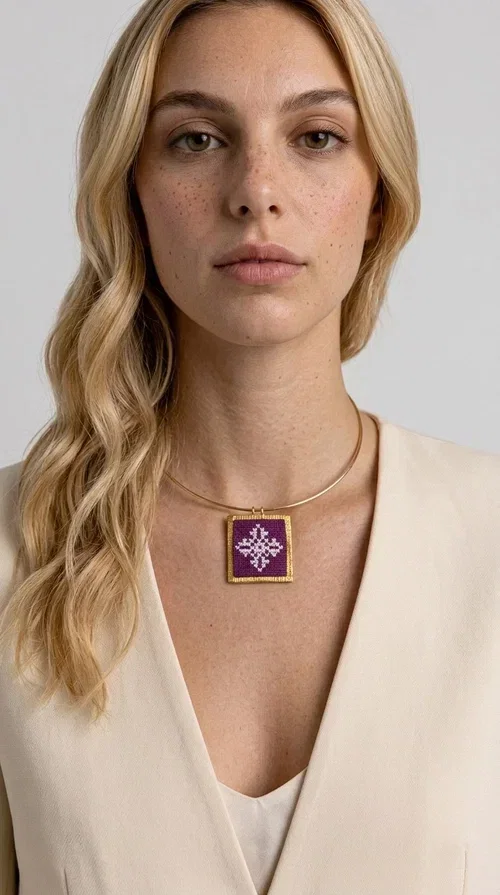 , The embroidered magenta necklace with geometric patterns is a statement piece that combines the traditional art of embroidery with a modern aesthetic — ideal for every woman who wants to express herself boldly and stylishly.

Designed by Greek Jewelry Designer Aikaterini Chalkiadaki, this handmade necklace features a square pendant in deep purple-magenta fabric, adorned with a white embroidered geometric design inspired by folk art tradition. The golden brass metal frame elegantly encases the pendant, while the delicate gold choker-style chain showcases it flawlessly around the neck. The result is a piece of jewelry with soul, character, and a strong visual presence.

Wear it over a white shirt, dress, or blazer to create a striking combination. It looks equally great in casual and more formal outfits, making it a versatile accessory for any occasion.