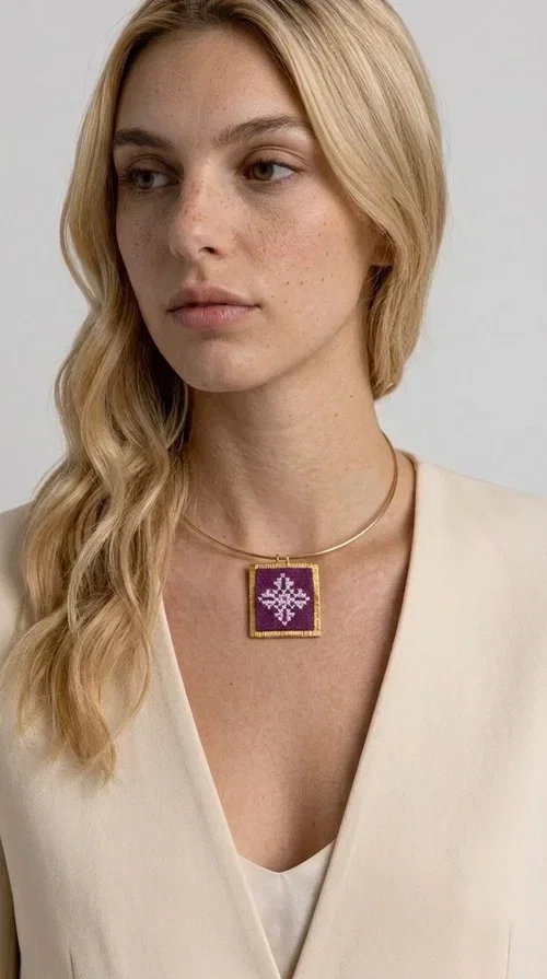, The embroidered magenta necklace with geometric patterns is a statement piece that combines the traditional art of embroidery with a modern aesthetic — ideal for every woman who wants to express herself boldly and stylishly.

Designed by Greek Jewelry Designer Aikaterini Chalkiadaki, this handmade necklace features a square pendant in deep purple-magenta fabric, adorned with a white embroidered geometric design inspired by folk art tradition. The golden brass metal frame elegantly encases the pendant, while the delicate gold choker-style chain showcases it flawlessly around the neck. The result is a piece of jewelry with soul, character, and a strong visual presence.

Wear it over a white shirt, dress, or blazer to create a striking combination. It looks equally great in casual and more formal outfits, making it a versatile accessory for any occasion.
