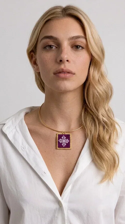 , The embroidered magenta necklace with geometric patterns is a statement piece that combines the traditional art of embroidery with a modern aesthetic — ideal for every woman who wants to express herself boldly and stylishly.

Designed by Greek Jewelry Designer Aikaterini Chalkiadaki, this handmade necklace features a square pendant in deep purple-magenta fabric, adorned with a white embroidered geometric design inspired by folk art tradition. The golden brass metal frame elegantly encases the pendant, while the delicate gold choker-style chain showcases it flawlessly around the neck. The result is a piece of jewelry with soul, character, and a strong visual presence.

Wear it over a white shirt, dress, or blazer to create a striking combination. It looks equally great in casual and more formal outfits, making it a versatile accessory for any occasion.