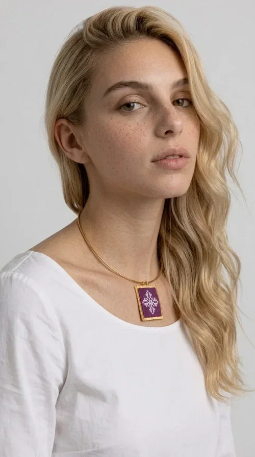 , The embroidered magenta necklace with geometric patterns is a statement piece that combines the traditional art of embroidery with a modern aesthetic — ideal for every woman who wants to express herself boldly and stylishly.

Designed by Greek Jewelry Designer Aikaterini Chalkiadaki, this handmade necklace features a square pendant in deep purple-magenta fabric, adorned with a white embroidered geometric design inspired by folk art tradition. The golden brass metal frame elegantly encases the pendant, while the delicate gold choker-style chain showcases it flawlessly around the neck. The result is a piece of jewelry with soul, character, and a strong visual presence.

Wear it over a white shirt, dress, or blazer to create a striking combination. It looks equally great in casual and more formal outfits, making it a versatile accessory for any occasion.