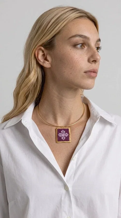 , The embroidered magenta necklace with geometric patterns is a statement piece that combines the traditional art of embroidery with a modern aesthetic — ideal for every woman who wants to express herself boldly and stylishly.

Designed by Greek Jewelry Designer Aikaterini Chalkiadaki, this handmade necklace features a square pendant in deep purple-magenta fabric, adorned with a white embroidered geometric design inspired by folk art tradition. The golden brass metal frame elegantly encases the pendant, while the delicate gold choker-style chain showcases it flawlessly around the neck. The result is a piece of jewelry with soul, character, and a strong visual presence.

Wear it over a white shirt, dress, or blazer to create a striking combination. It looks equally great in casual and more formal outfits, making it a versatile accessory for any occasion.