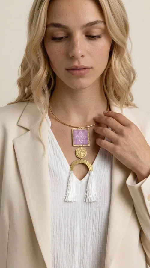 , A statement embroidered necklace that combines the traditional art of embroidery with a modern aesthetic — the ideal piece for every woman who wants to express herself with style and authenticity.

Designed by Greek Jewelry Designer Aikaterini Chalkiadaki, this handmade necklace features an embroidered square motif in pink/lilac tones with white geometric patterns inspired by Greek folk tradition. The embroidered piece is framed in golden brass and paired with a round embossed motif and a semicircular gold base, from which delicate white tassels hang, adding movement and grace. The look is completed with a fine gold choker-style chain.

Ideal to wear over a white top, a dress, or even a simple casual look that needs a touch of character. This striking long necklace turns any outfit into a true styling statement.