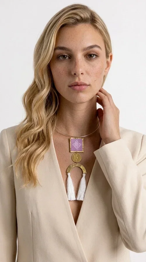, A statement embroidered necklace that combines the traditional art of embroidery with a modern aesthetic — the ideal piece for every woman who wants to express herself with style and authenticity.

Designed by Greek Jewelry Designer Aikaterini Chalkiadaki, this handmade necklace features an embroidered square motif in pink/lilac tones with white geometric patterns inspired by Greek folk tradition. The embroidered piece is framed in golden brass and paired with a round embossed motif and a semicircular gold base, from which delicate white tassels hang, adding movement and grace. The look is completed with a fine gold choker-style chain.

Ideal to wear over a white top, a dress, or even a simple casual look that needs a touch of character. This striking long necklace turns any outfit into a true styling statement.