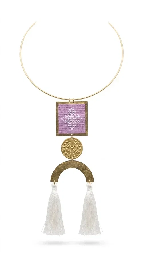 , A statement embroidered necklace that combines the traditional art of embroidery with a modern aesthetic — the ideal piece for every woman who wants to express herself with style and authenticity.

Designed by Greek Jewelry Designer Aikaterini Chalkiadaki, this handmade necklace features an embroidered square motif in pink/lilac tones with white geometric patterns inspired by Greek folk tradition. The embroidered piece is framed in golden brass and paired with a round embossed motif and a semicircular gold base, from which delicate white tassels hang, adding movement and grace. The look is completed with a fine gold choker-style chain.

Ideal to wear over a white top, a dress, or even a simple casual look that needs a touch of character. This striking long necklace turns any outfit into a true styling statement.