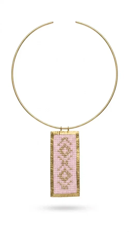 , The embroidered pink necklace with geometric patterns is a statement piece that combines the traditional art of embroidery with a modern, striking result. Designed by Greek Jewelry Designer Aikaterini Chalkiadaki, this unique necklace draws inspiration from folk tradition and the folk aesthetic that defines the Folklore Jewelry collection.

The embroidered rectangular pendant, in a soft pink shade, is adorned with gold geometric motifs reminiscent of traditional embroidery, while the gold brass metal frame gives it structure and elegance. It is worn on a delicate gold torque-style neck hoop that fits comfortably and instantly elevates any outfit, from casual to formal.

Ideal for women who love handmade jewelry with character, it is the perfect choice as a gift or to refresh your own jewelry collection with a piece full of soul.