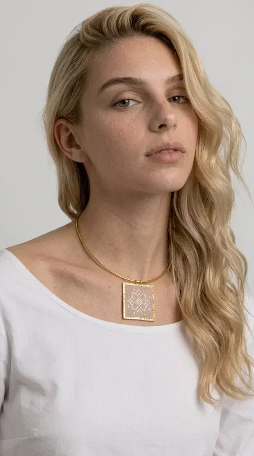 , The statement embroidered necklace in a pink hue is a piece of jewelry that combines the traditional art of embroidery with contemporary design, creating a result that immediately catches the eye. Designed by Aikaterini Chalkiadaki, it carries the signature of Greek handmade craftsmanship and is an ideal choice for those seeking jewelry with character and history.

The necklace features a rectangular embroidered pendant with geometric patterns inspired by folk art and a folklore aesthetic. The pink fabric base combined with golden brass details creates a harmonious contrast that highlights the handmade element. The gold-toned metal omega-style chain gives structure and elegance to the whole, while the pendant is framed by distinctive golden details that emphasize the craftsmanship.

Wear it over a white t-shirt for a casual look or pair it with a blazer for a professional or evening look — just as shown in the photo. It is a piece of jewelry that suits every style and makes an excellent gift idea.