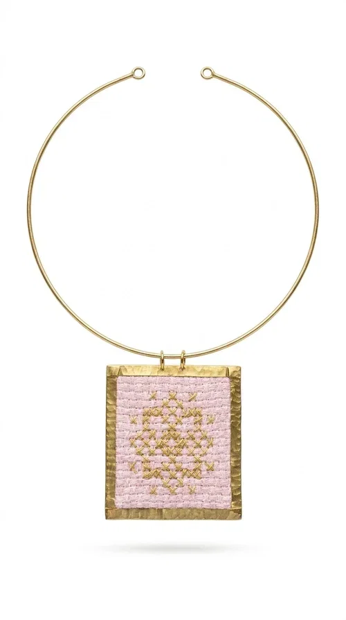 , The statement embroidered necklace in a pink hue is a piece of jewelry that combines the traditional art of embroidery with contemporary design, creating a result that immediately catches the eye. Designed by Aikaterini Chalkiadaki, it carries the signature of Greek handmade craftsmanship and is an ideal choice for those seeking jewelry with character and history.

The necklace features a rectangular embroidered pendant with geometric patterns inspired by folk art and a folklore aesthetic. The pink fabric base combined with golden brass details creates a harmonious contrast that highlights the handmade element. The gold-toned metal omega-style chain gives structure and elegance to the whole, while the pendant is framed by distinctive golden details that emphasize the craftsmanship.

Wear it over a white t-shirt for a casual look or pair it with a blazer for a professional or evening look — just as shown in the photo. It is a piece of jewelry that suits every style and makes an excellent gift idea.