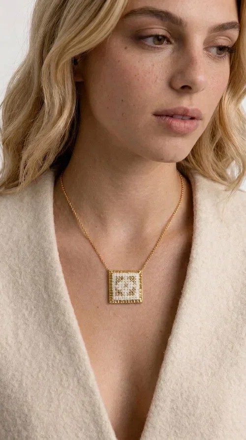 , The embroidered statement necklace with geometric patterns is a handmade piece of jewelry that combines the traditional art of embroidery with a modern, striking result. Designed by Greek Jewelry Designer Aikaterini Chalkiadaki, this unique necklace is an ideal choice for those who love jewelry with character and soul.

The pendant necklace features a square motif in white with detailed geometric embroidery, while the golden brass frame and delicate chain add elegance and a sense of luxury. The interplay of white fabric and gold details creates a look that suits both casual and formal outfits equally well.

Perfect as a gift or to complete your own look, this necklace pairs beautifully with white, ecru, or monochrome outfits. It can be worn alone as a statement piece or combined with thinner necklaces for a layered look.