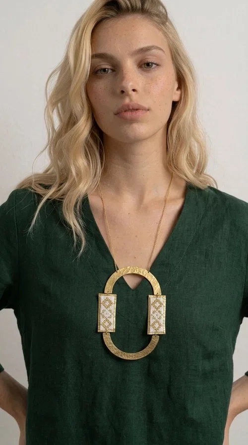 , An embroidered necklace that blends tradition with modern design — the Statement necklace KOL-4745 is the ideal choice for every woman who wants to express herself with style and authenticity.

Designed by Greek Jewelry Designer Aikaterini Chalkiadaki, this striking long necklace features a handmade oval brass element in a gold tone, framed by two rectangular embroidered plaques made of white fabric with geometric patterns inspired by Greek folk tradition. The gold-tone chain adds an elegant, modern touch, while the embroidered motifs bring a warm, handcrafted feel.

Perfect for pairing with simple outfits in neutral shades — such as khaki, white or beige — it turns any look into a true statement. Suitable for both everyday wear and special evening occasions.