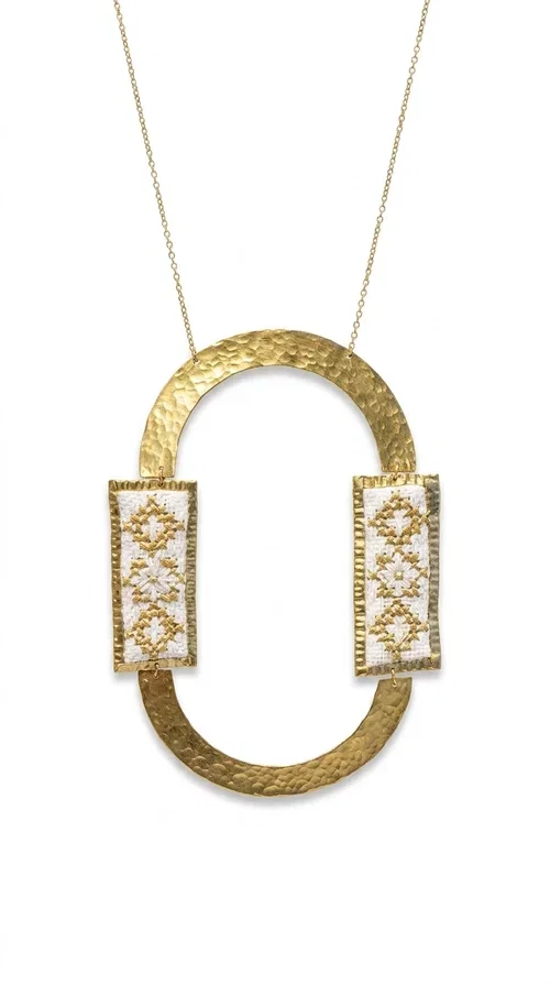 , An embroidered necklace that blends tradition with modern design — the Statement necklace KOL-4745 is the ideal choice for every woman who wants to express herself with style and authenticity.

Designed by Greek Jewelry Designer Aikaterini Chalkiadaki, this striking long necklace features a handmade oval brass element in a gold tone, framed by two rectangular embroidered plaques made of white fabric with geometric patterns inspired by Greek folk tradition. The gold-tone chain adds an elegant, modern touch, while the embroidered motifs bring a warm, handcrafted feel.

Perfect for pairing with simple outfits in neutral shades — such as khaki, white or beige — it turns any look into a true statement. Suitable for both everyday wear and special evening occasions.