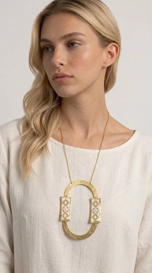 , An embroidered necklace that blends tradition with modern design — the Statement necklace KOL-4745 is the ideal choice for every woman who wants to express herself with style and authenticity.

Designed by Greek Jewelry Designer Aikaterini Chalkiadaki, this striking long necklace features a handmade oval brass element in a gold tone, framed by two rectangular embroidered plaques made of white fabric with geometric patterns inspired by Greek folk tradition. The gold-tone chain adds an elegant, modern touch, while the embroidered motifs bring a warm, handcrafted feel.

Perfect for pairing with simple outfits in neutral shades — such as khaki, white or beige — it turns any look into a true statement. Suitable for both everyday wear and special evening occasions.