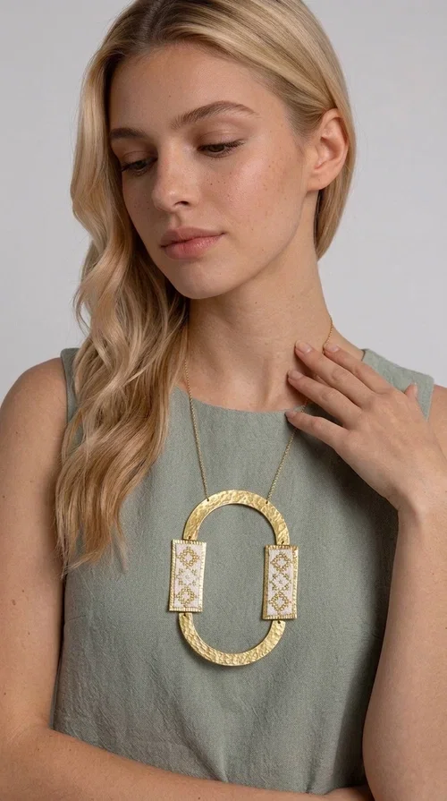 , An embroidered necklace that blends tradition with modern design — the Statement necklace KOL-4745 is the ideal choice for every woman who wants to express herself with style and authenticity.

Designed by Greek Jewelry Designer Aikaterini Chalkiadaki, this striking long necklace features a handmade oval brass element in a gold tone, framed by two rectangular embroidered plaques made of white fabric with geometric patterns inspired by Greek folk tradition. The gold-tone chain adds an elegant, modern touch, while the embroidered motifs bring a warm, handcrafted feel.

Perfect for pairing with simple outfits in neutral shades — such as khaki, white or beige — it turns any look into a true statement. Suitable for both everyday wear and special evening occasions.