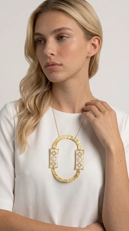 , An embroidered necklace that blends tradition with modern design — the Statement necklace KOL-4745 is the ideal choice for every woman who wants to express herself with style and authenticity.

Designed by Greek Jewelry Designer Aikaterini Chalkiadaki, this striking long necklace features a handmade oval brass element in a gold tone, framed by two rectangular embroidered plaques made of white fabric with geometric patterns inspired by Greek folk tradition. The gold-tone chain adds an elegant, modern touch, while the embroidered motifs bring a warm, handcrafted feel.

Perfect for pairing with simple outfits in neutral shades — such as khaki, white or beige — it turns any look into a true statement. Suitable for both everyday wear and special evening occasions.