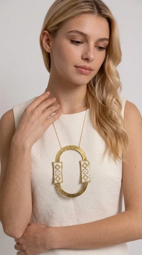 , An embroidered necklace that blends tradition with modern design — the Statement necklace KOL-4745 is the ideal choice for every woman who wants to express herself with style and authenticity.

Designed by Greek Jewelry Designer Aikaterini Chalkiadaki, this striking long necklace features a handmade oval brass element in a gold tone, framed by two rectangular embroidered plaques made of white fabric with geometric patterns inspired by Greek folk tradition. The gold-tone chain adds an elegant, modern touch, while the embroidered motifs bring a warm, handcrafted feel.

Perfect for pairing with simple outfits in neutral shades — such as khaki, white or beige — it turns any look into a true statement. Suitable for both everyday wear and special evening occasions.