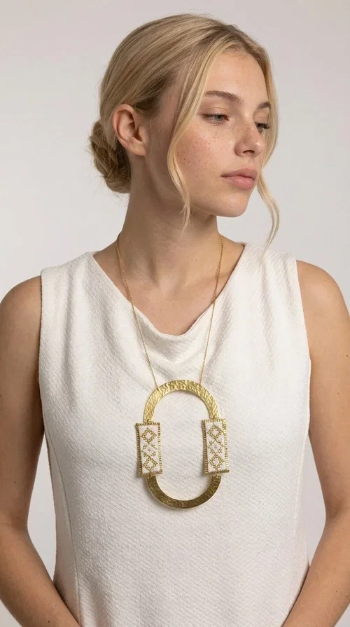 , An embroidered necklace that blends tradition with modern design — the Statement necklace KOL-4745 is the ideal choice for every woman who wants to express herself with style and authenticity.

Designed by Greek Jewelry Designer Aikaterini Chalkiadaki, this striking long necklace features a handmade oval brass element in a gold tone, framed by two rectangular embroidered plaques made of white fabric with geometric patterns inspired by Greek folk tradition. The gold-tone chain adds an elegant, modern touch, while the embroidered motifs bring a warm, handcrafted feel.

Perfect for pairing with simple outfits in neutral shades — such as khaki, white or beige — it turns any look into a true statement. Suitable for both everyday wear and special evening occasions.