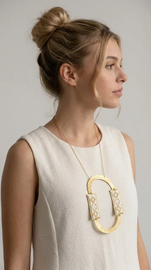 , An embroidered necklace that blends tradition with modern design — the Statement necklace KOL-4745 is the ideal choice for every woman who wants to express herself with style and authenticity.

Designed by Greek Jewelry Designer Aikaterini Chalkiadaki, this striking long necklace features a handmade oval brass element in a gold tone, framed by two rectangular embroidered plaques made of white fabric with geometric patterns inspired by Greek folk tradition. The gold-tone chain adds an elegant, modern touch, while the embroidered motifs bring a warm, handcrafted feel.

Perfect for pairing with simple outfits in neutral shades — such as khaki, white or beige — it turns any look into a true statement. Suitable for both everyday wear and special evening occasions.