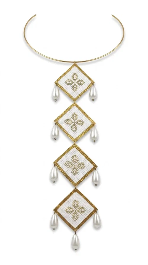 , An embroidered statement necklace that instantly catches the eye — featuring geometric patterns inspired by Greek tradition and an aesthetic that speaks to both the past and the present.

Designed by Greek Jewelry Designer Aikaterini Chalkiadaki, this statement necklace combines white embroidered fabric with gold brass and white pearls in a composition reminiscent of folklore art with a contemporary touch. Four diamond-shaped embroidered elements are stacked vertically, one beneath the other, with teardrop pearls gracefully hanging from each corner. The piece is completed with a delicate gold rigid choker, giving it an airy yet striking presence.

Ideal for women who love long, eye-catching necklaces with a distinctive identity. It pairs perfectly with simple, solid-colored outfits — just as shown in the photo with the pink sleeveless top — or with boho looks for festivals and summer outings. It can also be combined with matching necklace and earring sets for a complete look.